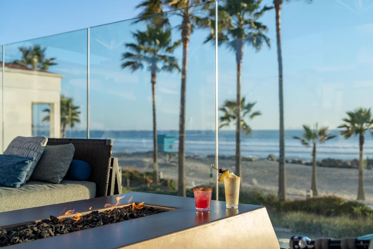 A fire pit and two drinks on Hotel del Coronado’s Sun Deck overlooking the beach and palm trees