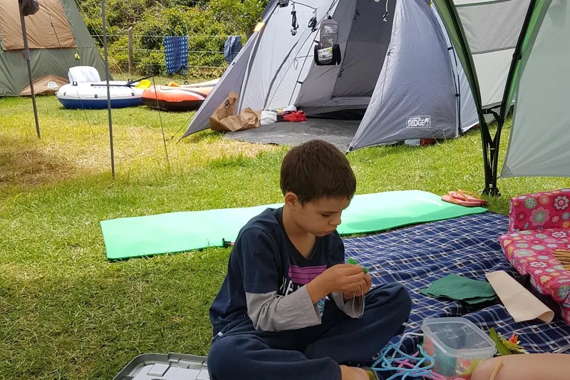 Child doing crafts under a camping awning with several tents behind